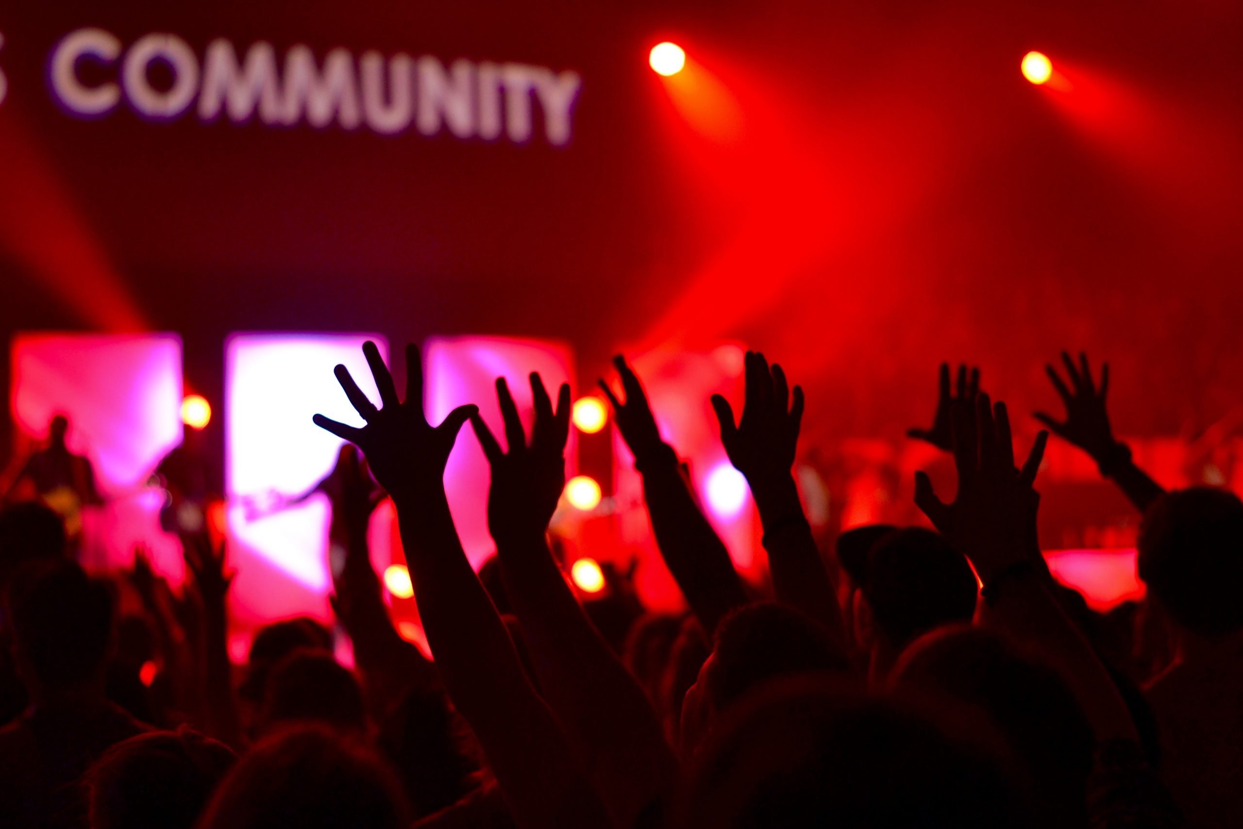 The image shows a nightclub environment with the word community above a bunch of raised hands.